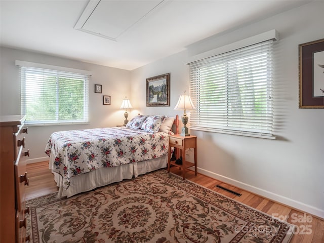 bedroom with visible vents, attic access, baseboards, and wood finished floors