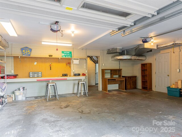 garage with a garage door opener, a workshop area, and concrete block wall