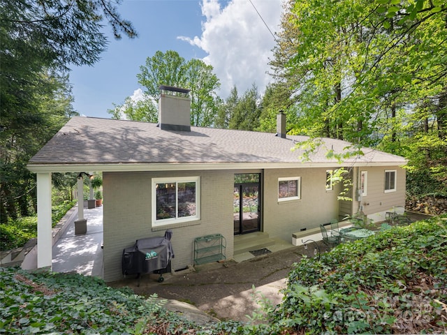 rear view of property featuring roof with shingles, a chimney, and brick siding