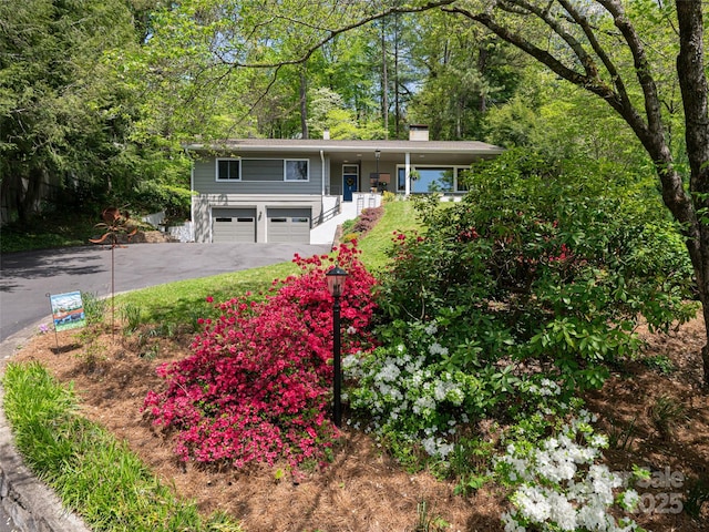 split foyer home featuring a garage, aphalt driveway, covered porch, and a chimney