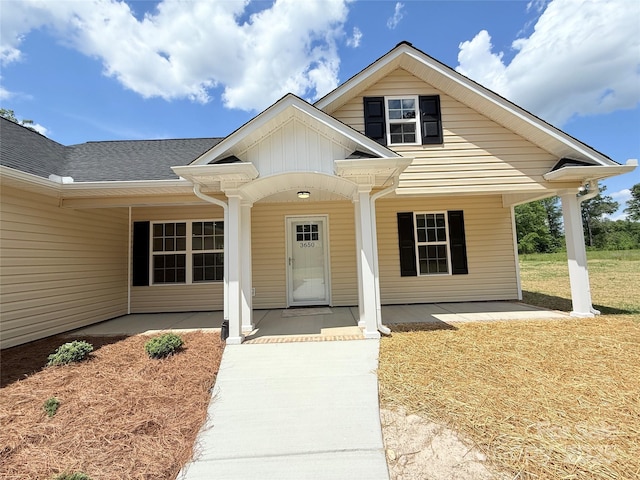 view of exterior entry with covered porch, board and batten siding, and roof with shingles