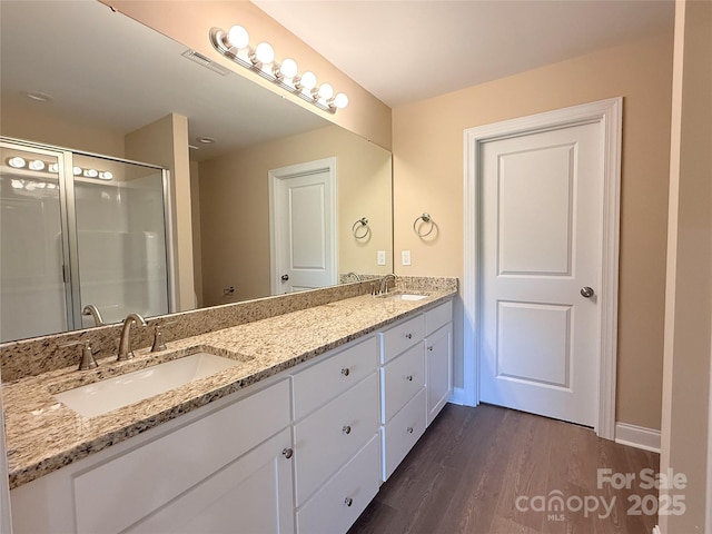 full bathroom with a sink, double vanity, a stall shower, and wood finished floors