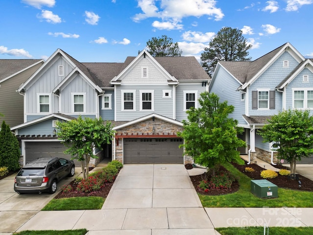 view of front facade with board and batten siding, driveway, a garage, stone siding, and a shingled roof