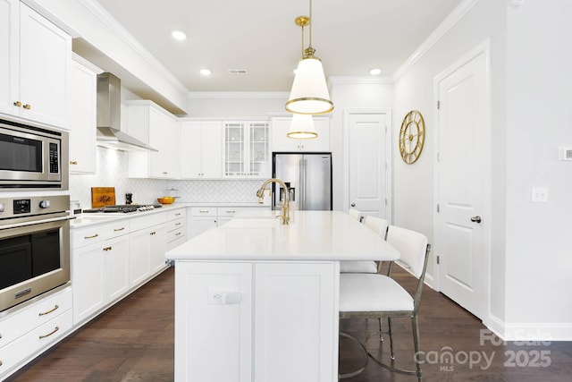kitchen featuring stainless steel appliances, wall chimney range hood, a sink, a kitchen bar, and crown molding