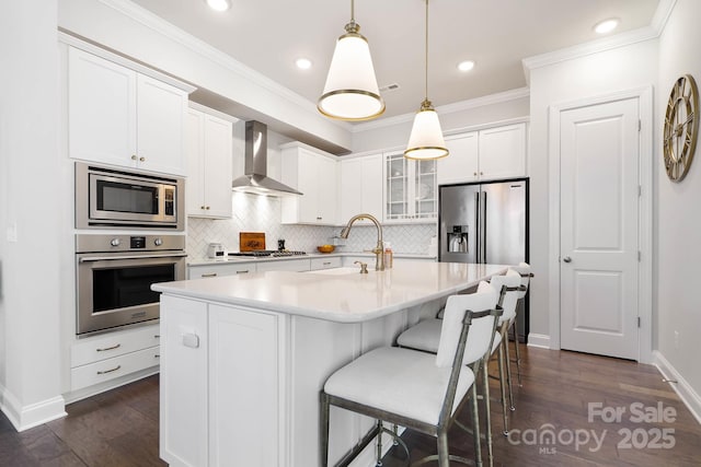 kitchen with stainless steel appliances, wall chimney range hood, a sink, decorative backsplash, and white cabinets