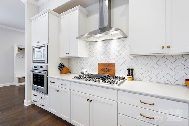 kitchen with wall chimney range hood, appliances with stainless steel finishes, crown molding, backsplash, and white cabinets