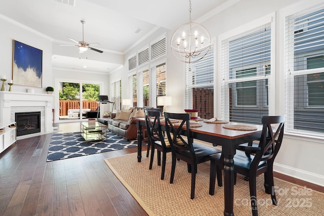 dining room featuring dark wood-style flooring, a chandelier, a glass covered fireplace, ceiling fan, and ornamental molding