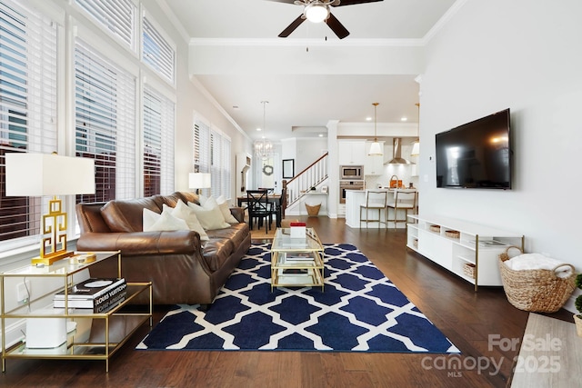 living room with stairway, ceiling fan, dark wood finished floors, crown molding, and a chandelier