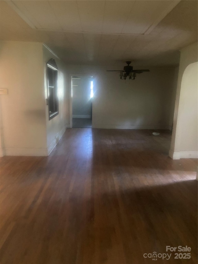 hall featuring arched walkways, baseboards, and wood finished floors