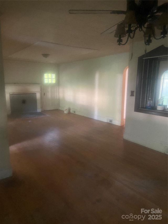 unfurnished living room featuring baseboards, arched walkways, a ceiling fan, and wood finished floors