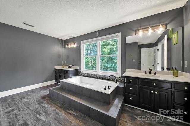8524 Quarters Ln, Mint Hill, NC 28227 - bathroom featuring wood finished floors, two vanities, a textured ceiling, a garden tub, and baseboards