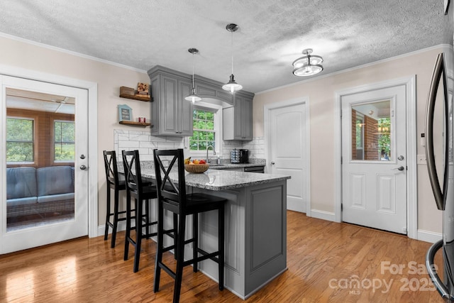 kitchen with a textured ceiling, a peninsula, light wood-type flooring, a kitchen bar, and gray cabinetry