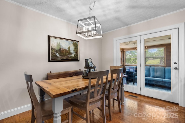 dining area with a textured ceiling, visible vents, wood finished floors, a notable chandelier, and ornamental molding