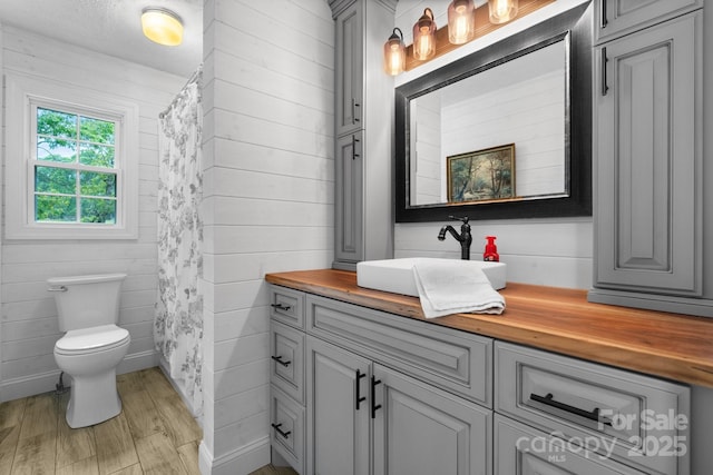 full bath with toilet, wood walls, wood finished floors, and vanity