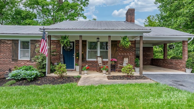 view of front of property featuring brick siding, metal roof, a porch, driveway, and a carport