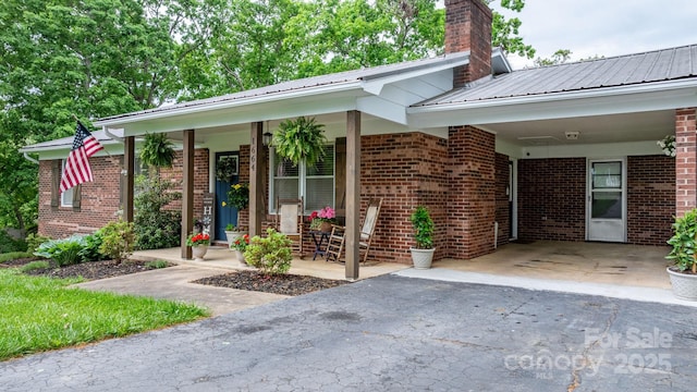doorway to property featuring an attached carport, brick siding, a chimney, and aphalt driveway