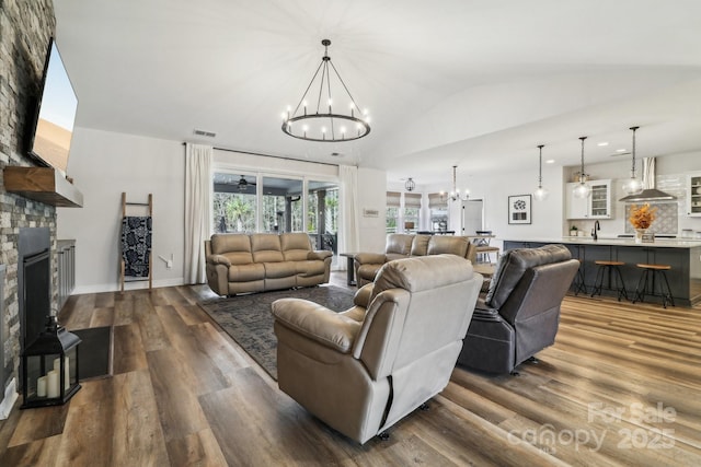 living area featuring visible vents, lofted ceiling, a fireplace, dark wood-style floors, and a chandelier