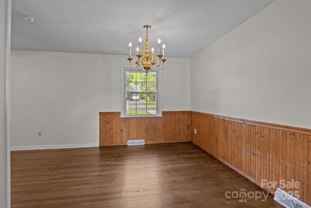 unfurnished room featuring a textured ceiling, wood walls, dark wood finished floors, a wainscoted wall, and an inviting chandelier