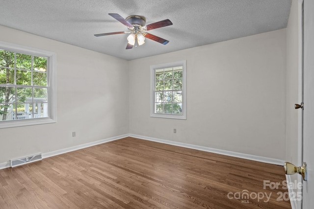 empty room featuring baseboards, visible vents, a wealth of natural light, and wood finished floors