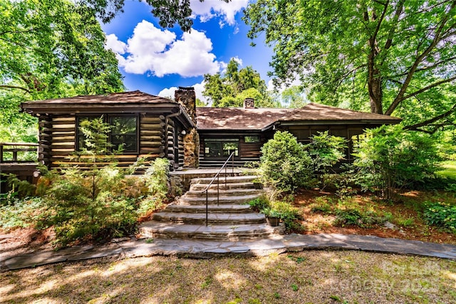 view of front of property featuring log exterior, a chimney, and stairs