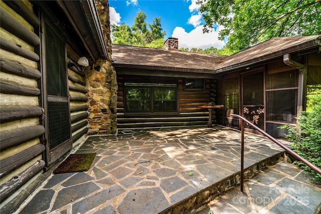 doorway to property featuring log siding, a chimney, and roof with shingles