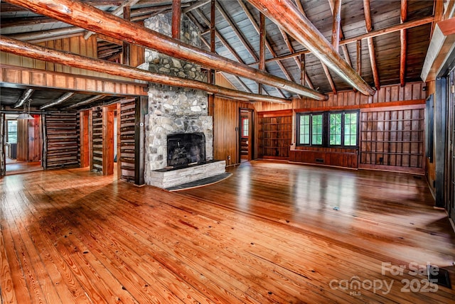 unfurnished living room with hardwood / wood-style flooring, high vaulted ceiling, healthy amount of natural light, wooden walls, and a fireplace