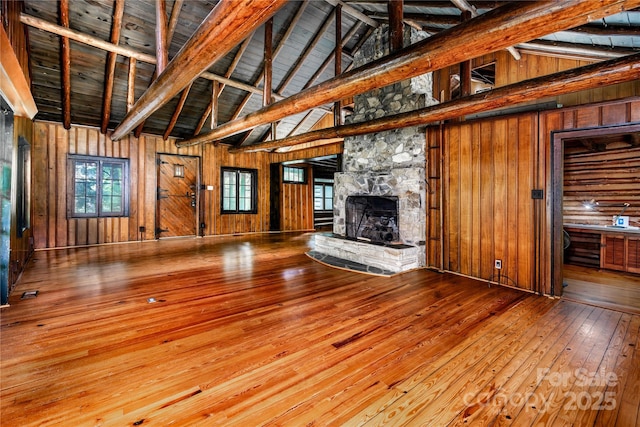 unfurnished living room with wood walls, hardwood / wood-style flooring, plenty of natural light, high vaulted ceiling, and a fireplace
