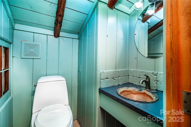 bathroom with toilet, vanity, and beamed ceiling