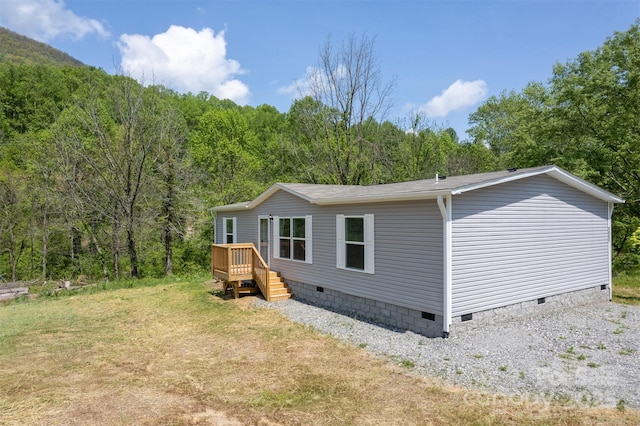 view of side of property featuring a wooded view, crawl space, and a deck