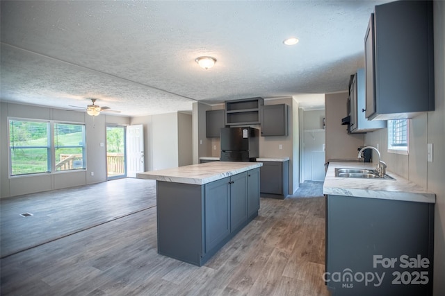 kitchen featuring open shelves, a sink, freestanding refrigerator, a healthy amount of sunlight, and a kitchen island