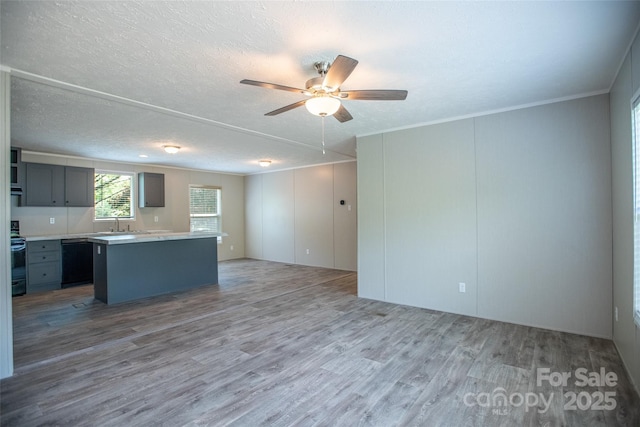 interior space with wood finished floors, a kitchen island, ceiling fan, light countertops, and dishwasher