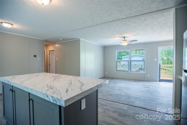 kitchen with wood finished floors, a kitchen island, open floor plan, ceiling fan, and a textured ceiling