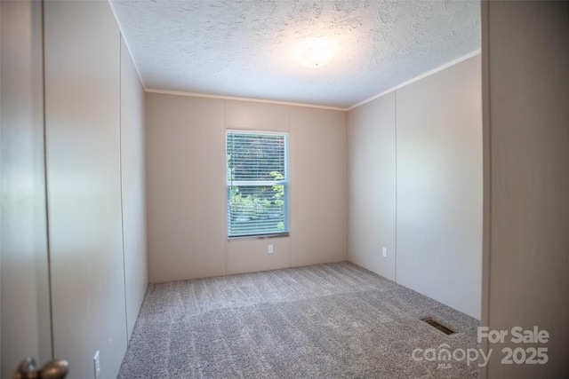 carpeted empty room featuring visible vents, ornamental molding, and a textured ceiling