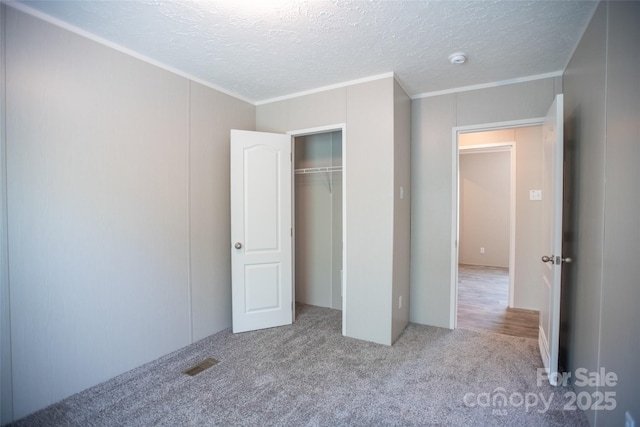 unfurnished bedroom featuring crown molding, a textured ceiling, carpet floors, and a closet