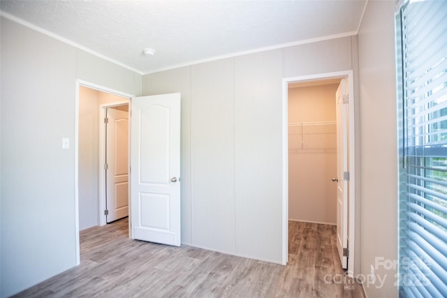 unfurnished bedroom featuring ornamental molding, a walk in closet, and wood finished floors