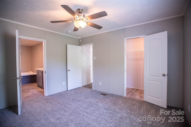unfurnished bedroom with crown molding, a walk in closet, and carpet flooring