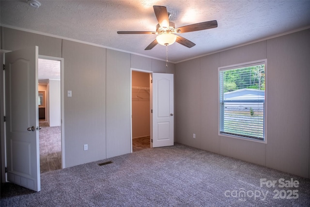unfurnished bedroom featuring ornamental molding, carpet, a textured ceiling, and a spacious closet