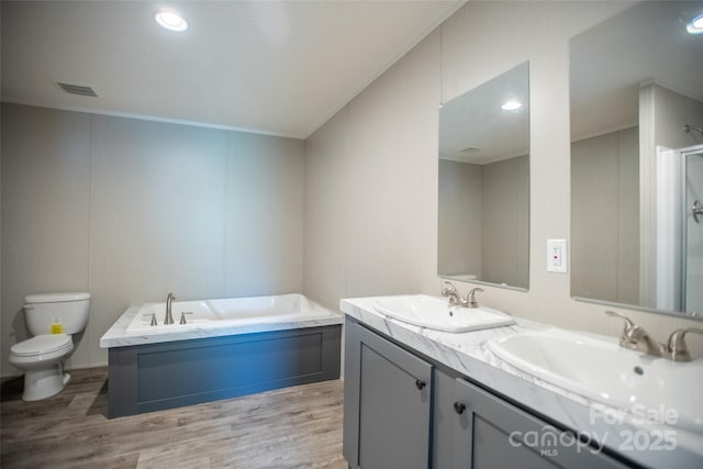 bathroom with a sink, toilet, wood finished floors, visible vents, and a bath