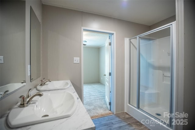 bathroom with double vanity, a shower stall, a sink, and wood finished floors