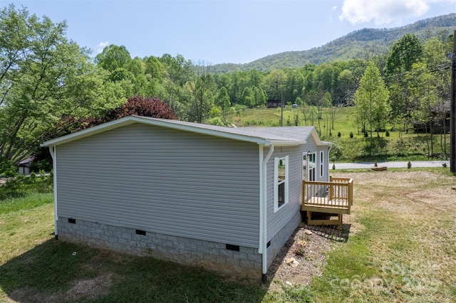 view of side of home featuring a yard, crawl space, a wooded view, and a mountain view
