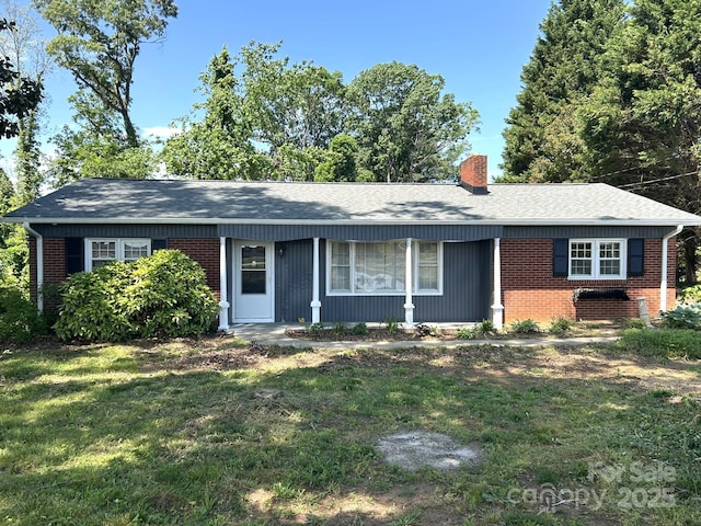 ranch-style home featuring brick siding, roof with shingles, a chimney, and a front yard