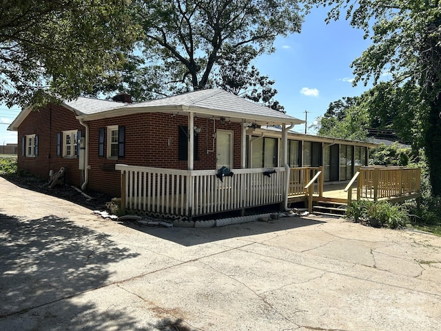 view of front of home featuring a sunroom, a wooden deck, and brick siding