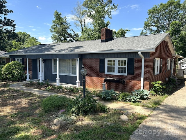 ranch-style house with a chimney, brick siding, a shingled roof, and covered porch