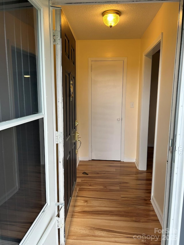 hall with light wood finished floors, baseboards, and a textured ceiling