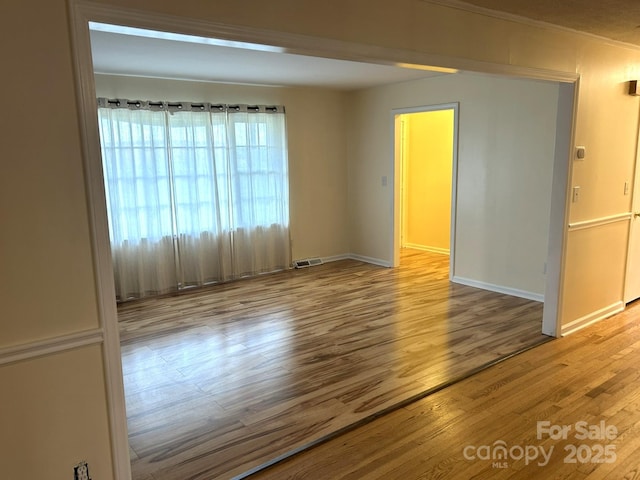spare room featuring wood finished floors, baseboards, and crown molding