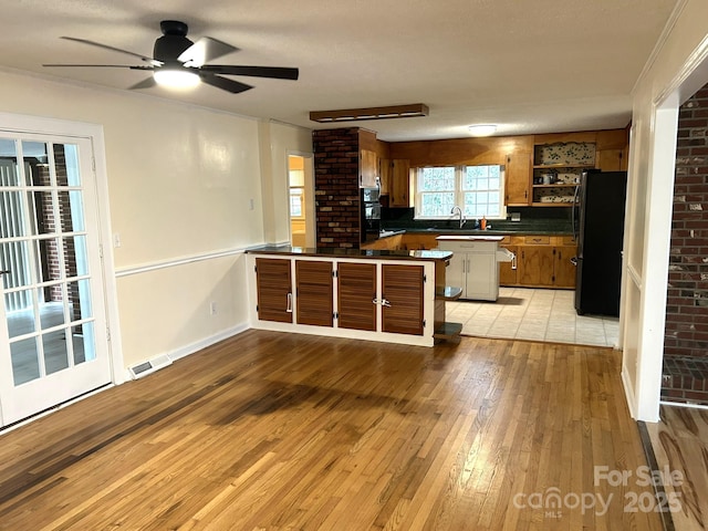 kitchen featuring freestanding refrigerator, open shelves, brown cabinetry, light wood-style floors, and a peninsula