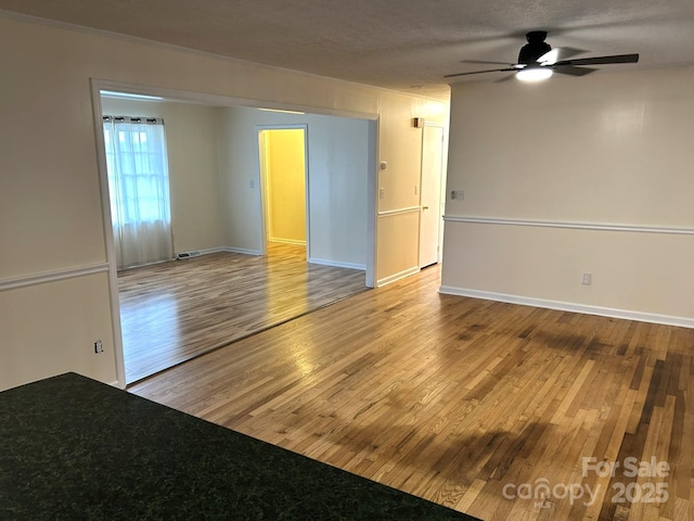 empty room with wood finished floors, a ceiling fan, and baseboards