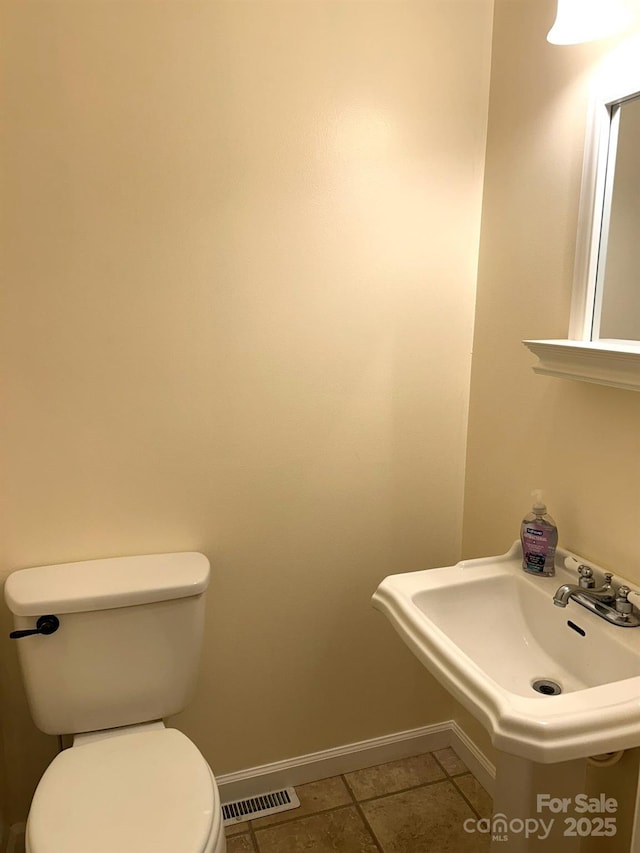 half bath with baseboards, toilet, a sink, and tile patterned floors