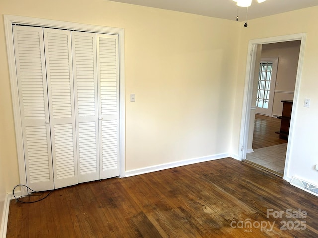 unfurnished bedroom with dark wood finished floors, a closet, and baseboards