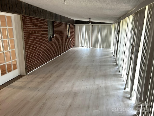 empty room with brick wall, light wood-type flooring, and a textured ceiling